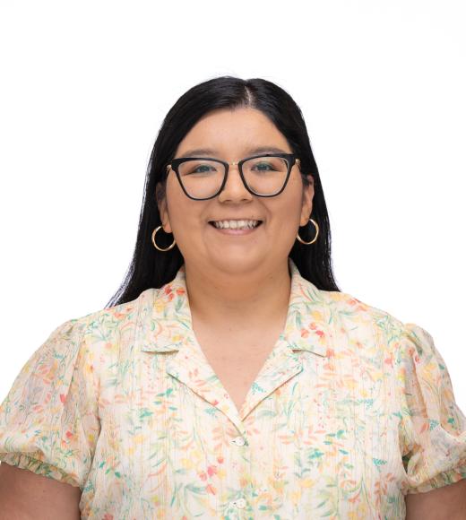 Maria is wearing a light floral shirt and smiling at the camera